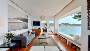 Un salon moderne avec un grand tableau, un téléviseur à écran plat, un coin repas et une vue sur la mer.