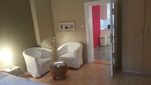 A hotel room with two white armchairs, a small round table, a bed, and a wardrobe.