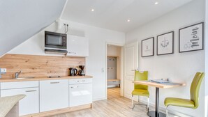Een moderne keuken met witte kasten, een houten aanrecht en een ingebouwde magnetron. Er is een eethoek met een tafel en twee stoelen.
