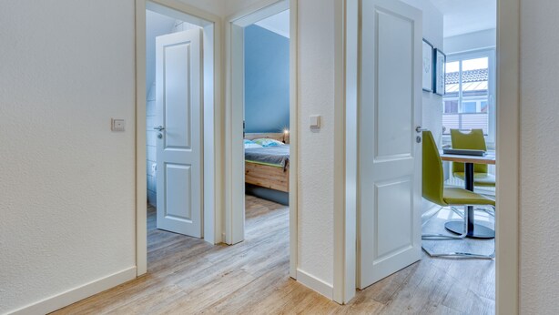 Een gang met twee open deuren die leiden naar een slaapkamer en een eetruimte.