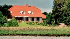 A house with a red roof, large windows, and a porch. - Apartment 1 Rosenträger - Apartments Rosenträger (Kappeln)