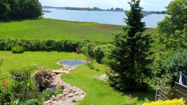 A lush green landscape with a pond, a wooden deck, and a view of a lake. - Apartment 1 Rosenträger - Apartments Rosenträger (Kappeln)