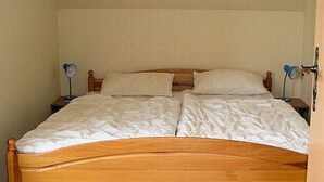 A double bed with white linens in a room with plain walls and a wooden headboard. - Apartment 1 Rosenträger - Apartments Rosenträger (Kappeln)