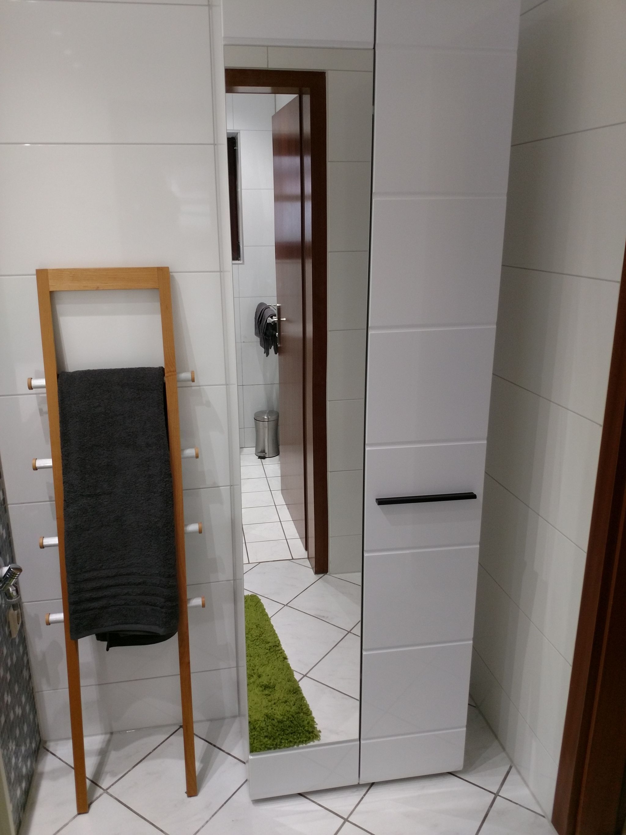 Ein Badezimmer mit einem hölzernen Handtuchhalter, einem weißen Schrank und einem grünen Teppich.