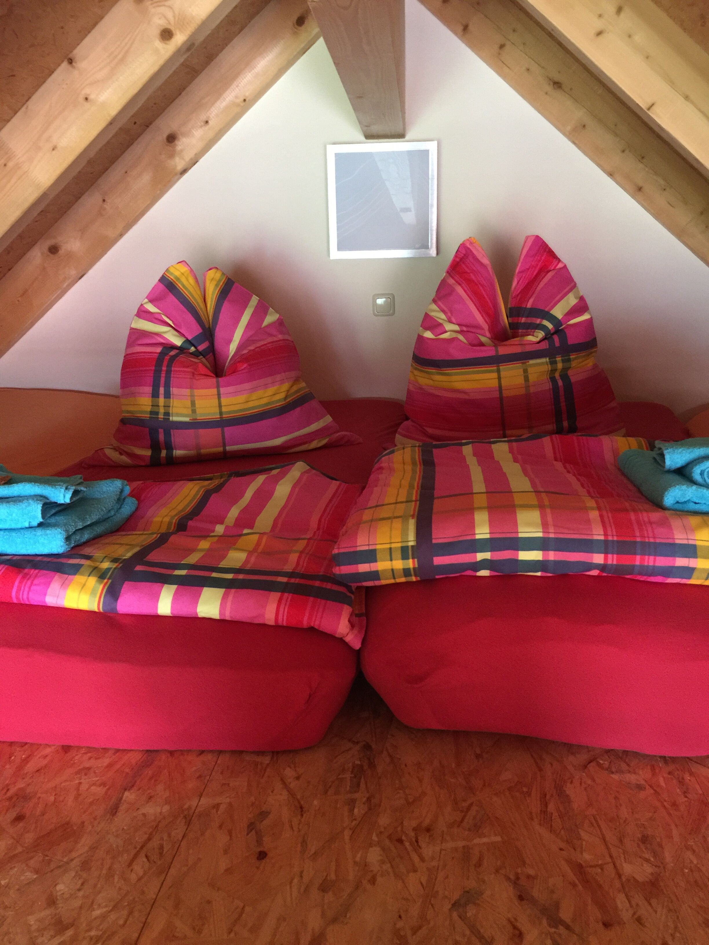Een gezellig slaapkamer onder het dak met twee rode bedden, kleurrijke streepjesbeddengoed en een houten plafond.