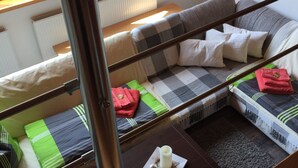 L’intérieur d’un chalet accueillant, avec un canapé, une petite table sur laquelle est posée une bougie, et une vue sur la verdure à l’extérieur.