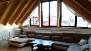 Un salon moderne avec un canapé d’angle, une table basse et une vue sur les immeubles à travers de grandes fenêtres.