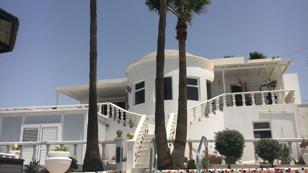 A pool area with a white building in the background, palm trees, and a staircase leading to the building.