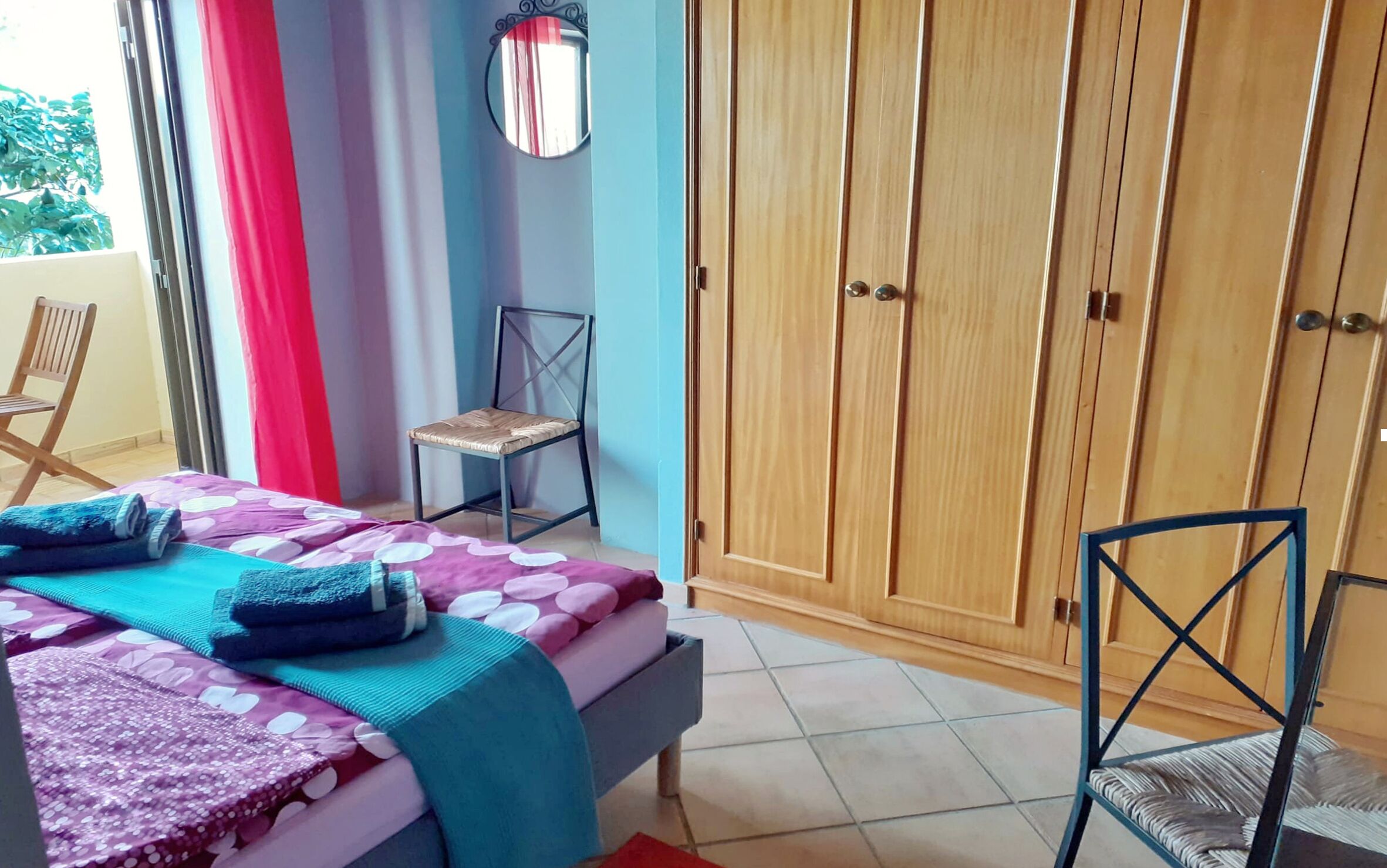 Un dormitorio con cama, una silla, un armario y una ventana con cortinas.