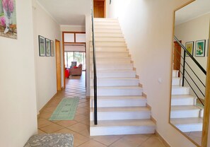 Eine Treppe führt zu einer zweiten Etage, mit Handlauf, einer grünen Matte auf dem Boden und gerahmten Bildern an den Wänden.