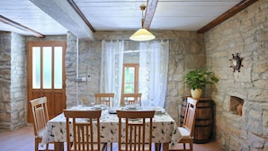 Un coin repas rustique avec un mur en pierre, des poutres en bois au plafond et une table dressée pour quatre personnes.