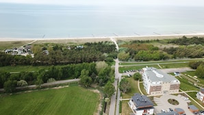 Luftaufnahme einer Küstenregion mit Strand, einer Straße und einem mehrstöckigen Gebäude mit Parkplatz.