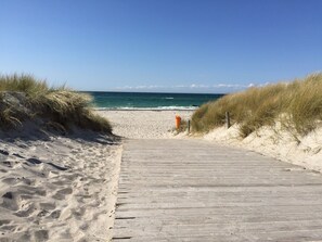 Une promenade en bois mène à une plage de sable bordée de dunes de chaque côté.