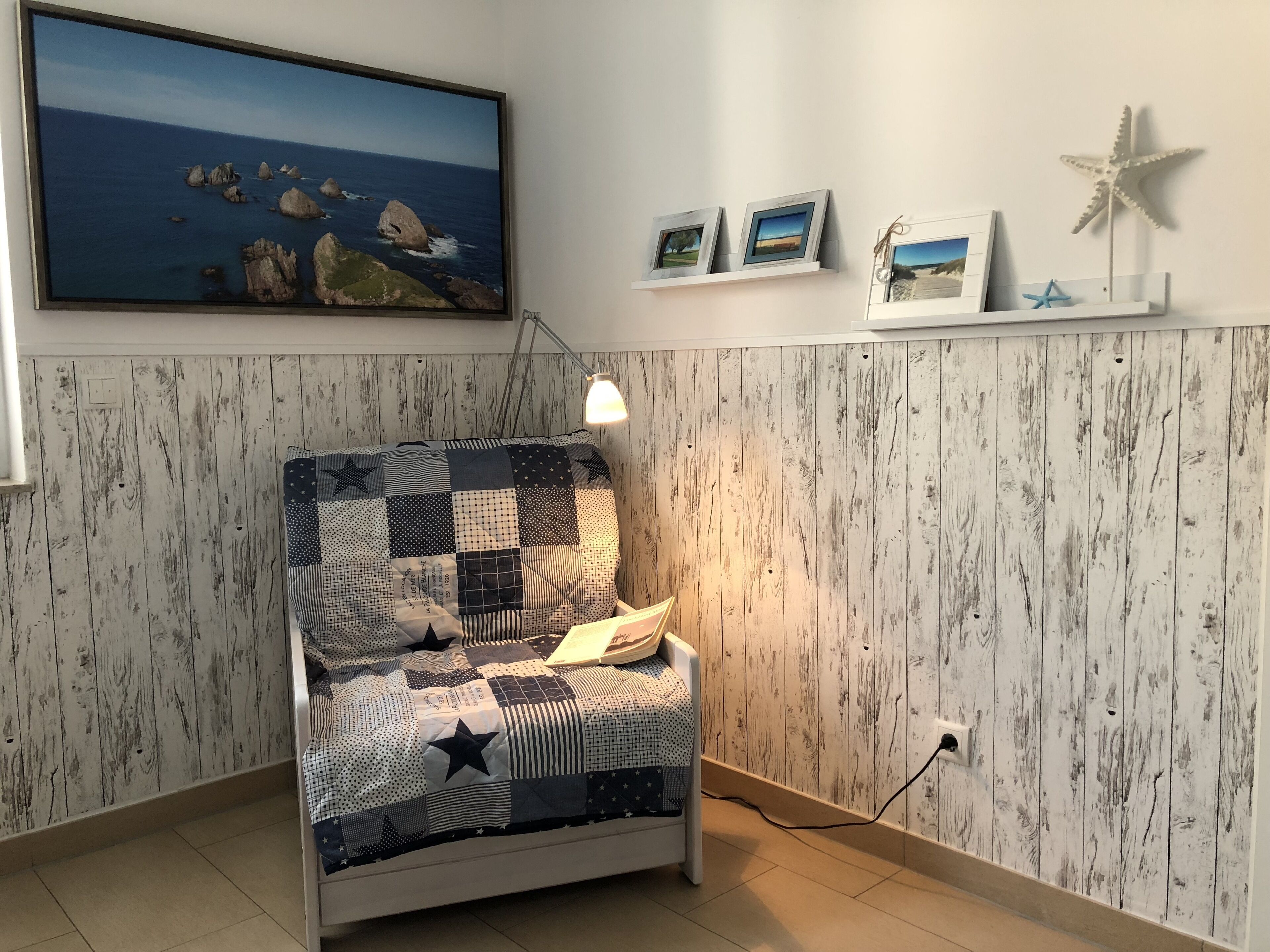 A cozy room with a wooden wall panel, a bed with a patchwork quilt, a framed picture of the ocean, and a starfish decoration.