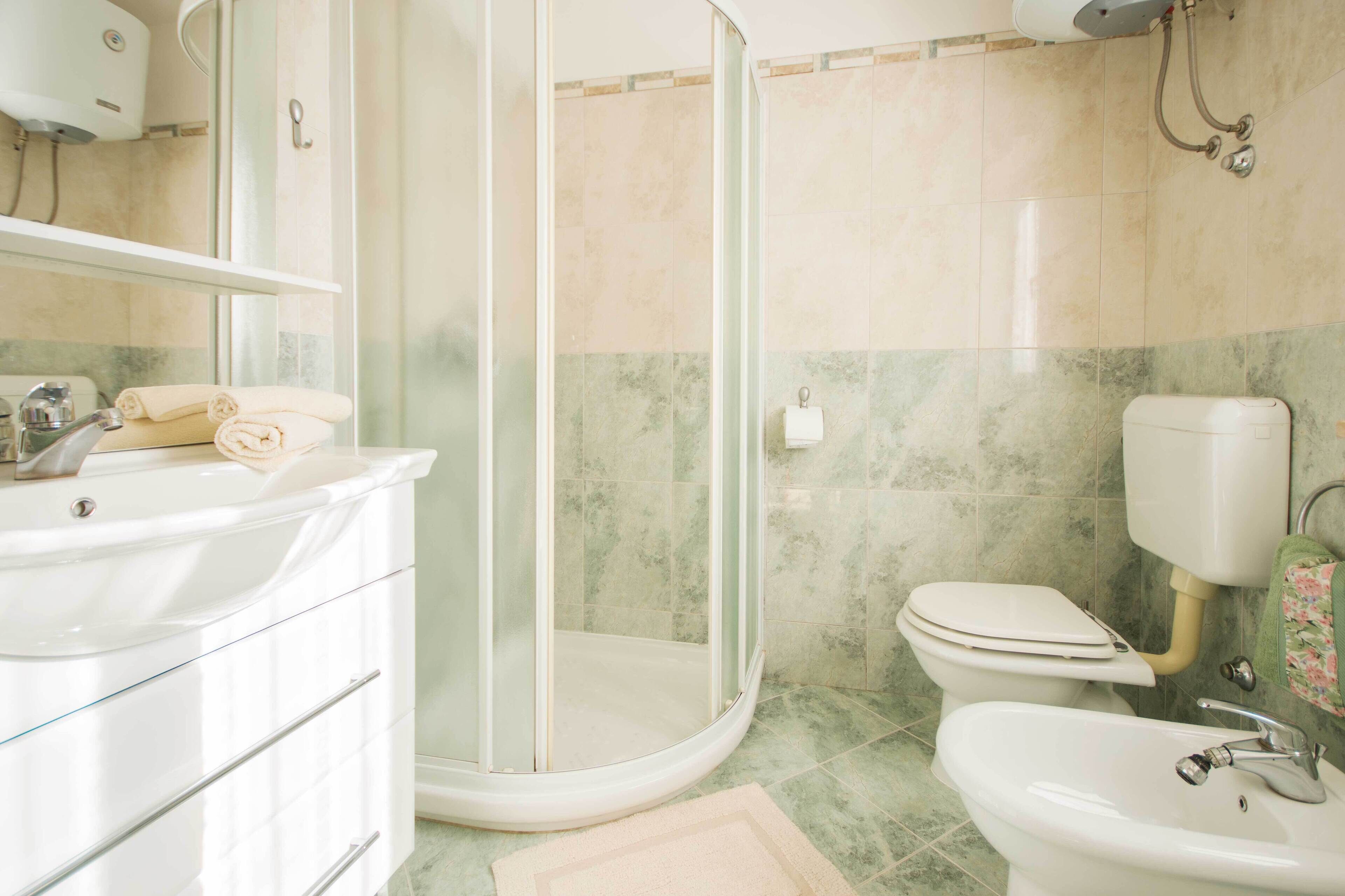 A bathroom with a glass-enclosed shower, a toilet, a sink, and a mirror above the sink.