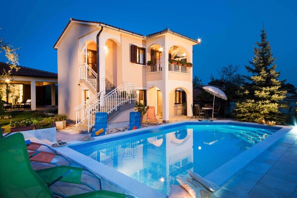 A two-story house with a swimming pool, outdoor furniture, and a staircase leading to the upper floor.