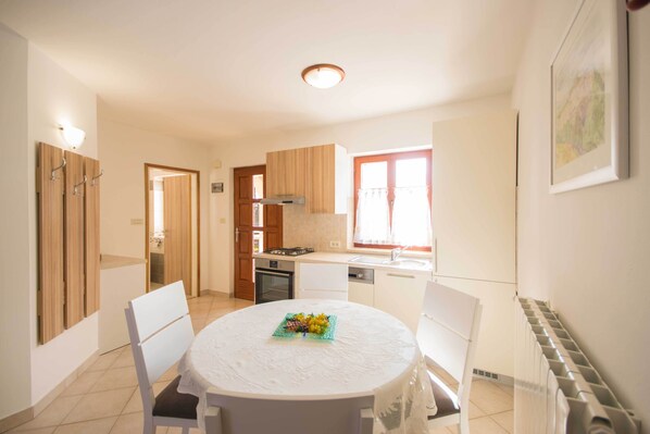 A compact kitchen with wooden cabinets, a round dining table with chairs, and a window with curtains.