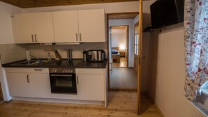 A compact kitchen with white cabinets, a built-in oven, and a countertop with a kettle and utensils. - Apartment with terrace, in the heart of the Elbe Sandstone Mountains, ideal for hiking (Bad Schandau)