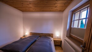 A bedroom with two single beds, wooden ceiling, a window with blinds, a radiator, and bedside lamps. - Apartment with terrace, in the heart of the Elbe Sandstone Mountains, ideal for hiking (Bad Schandau)