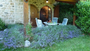 A stone building with a wooden pergola, two white wicker chairs, a table with a bottle, and a bowl of fruit. - Special prices in autumn! Charming apartment with large, heated pool (Rosières)