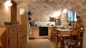 A rustic kitchen with wooden cabinets, a tiled floor, and a stone wall. - Special prices in autumn! Charming apartment with large, heated pool (Rosières)