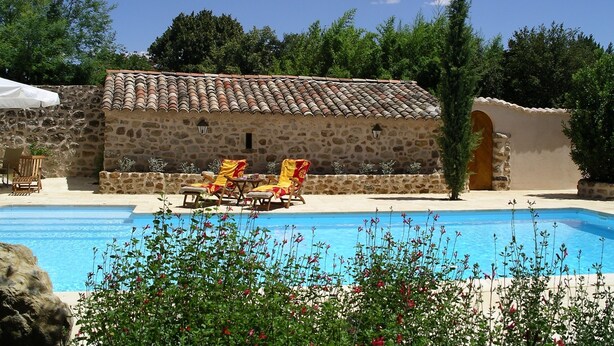A stone building with a tiled roof, a swimming pool, and outdoor seating with umbrellas. - Special prices in autumn! Charming apartment with large, heated pool (Rosières)