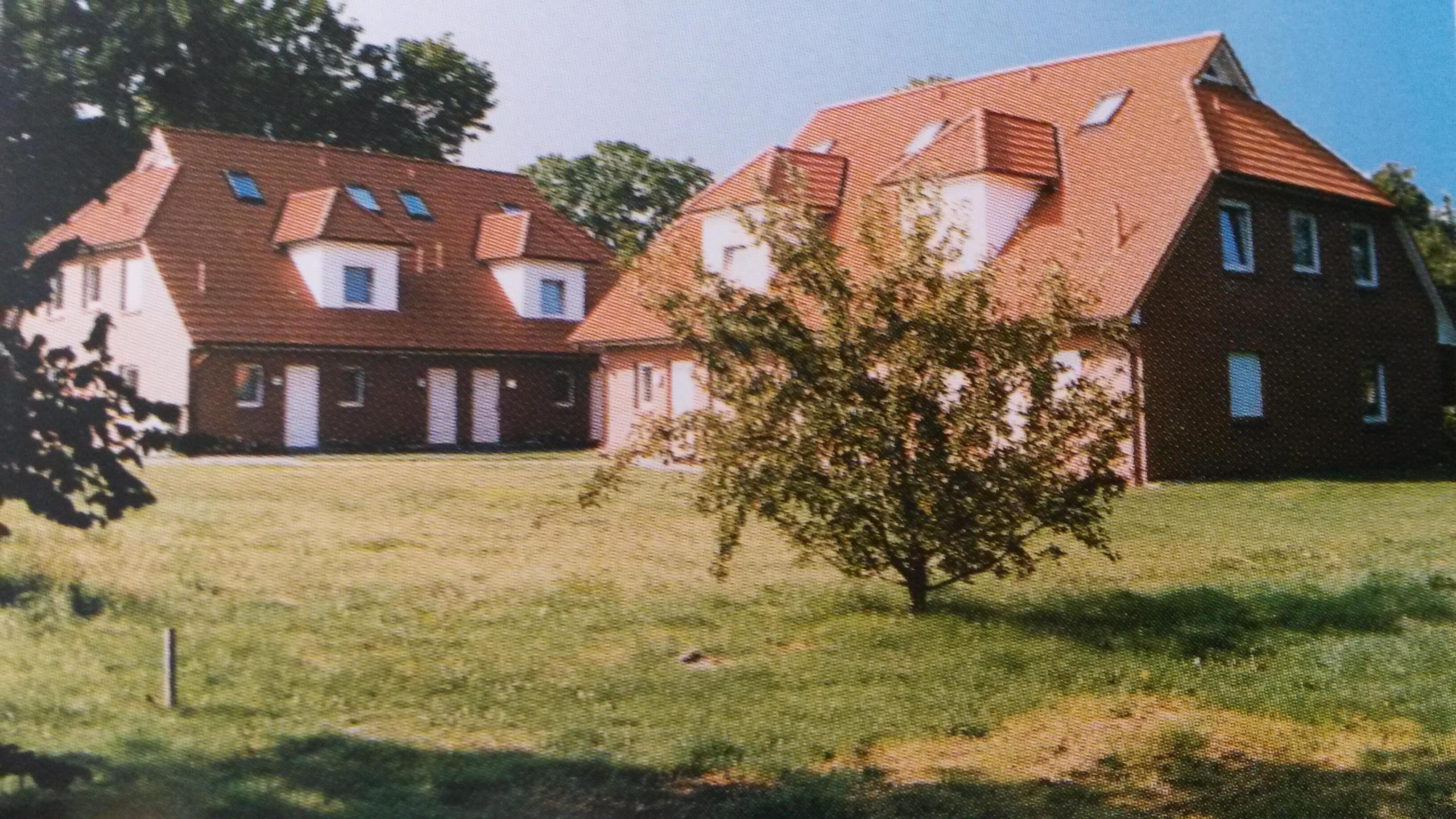 A two-story house with a red roof and white walls, surrounded by a grassy lawn.