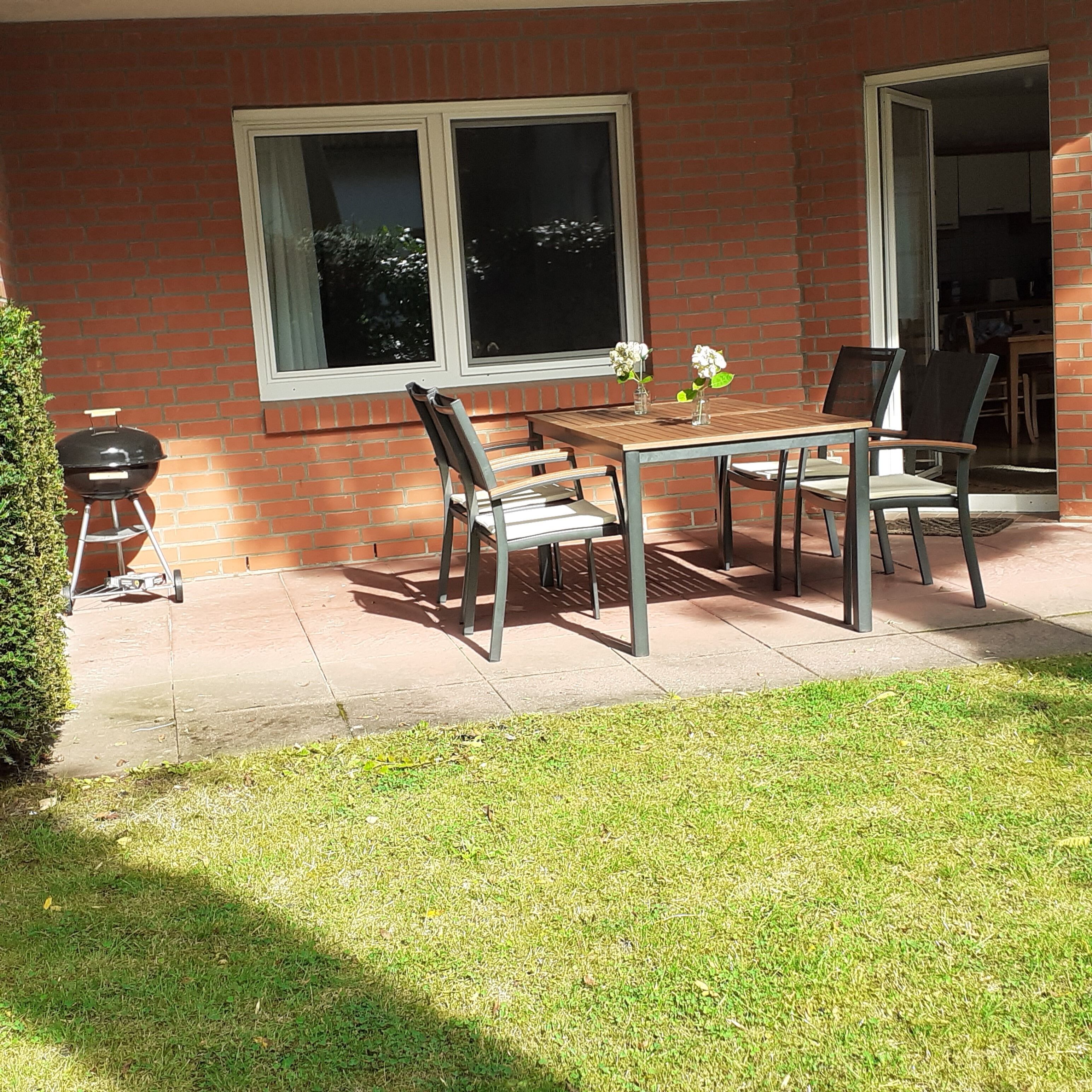 Un patio con mesa y sillas, una parrilla y una ventana.
