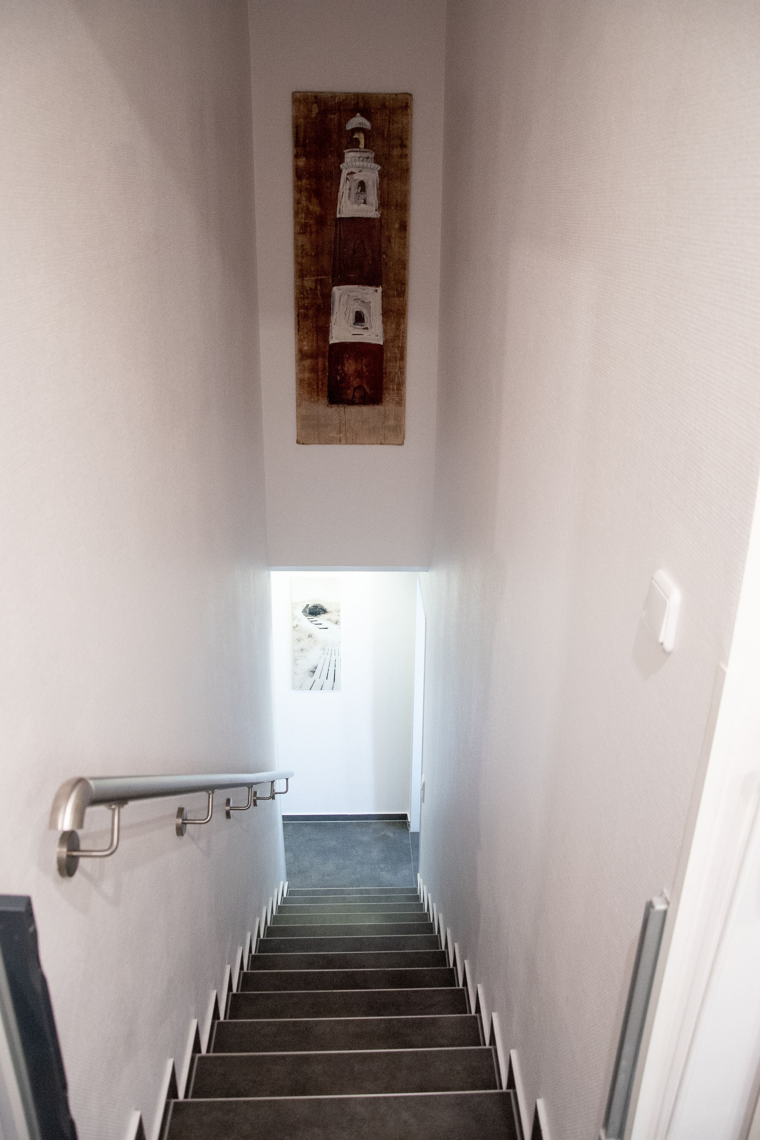 Una escalera con barandilla, una obra de arte en la pared y una puerta al final.