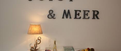 Eine Wand mit der Aufschrift 'JUIST & MEER', ein kleiner Tisch mit einer Lampe, einer Flasche und einer Fruchtschale.