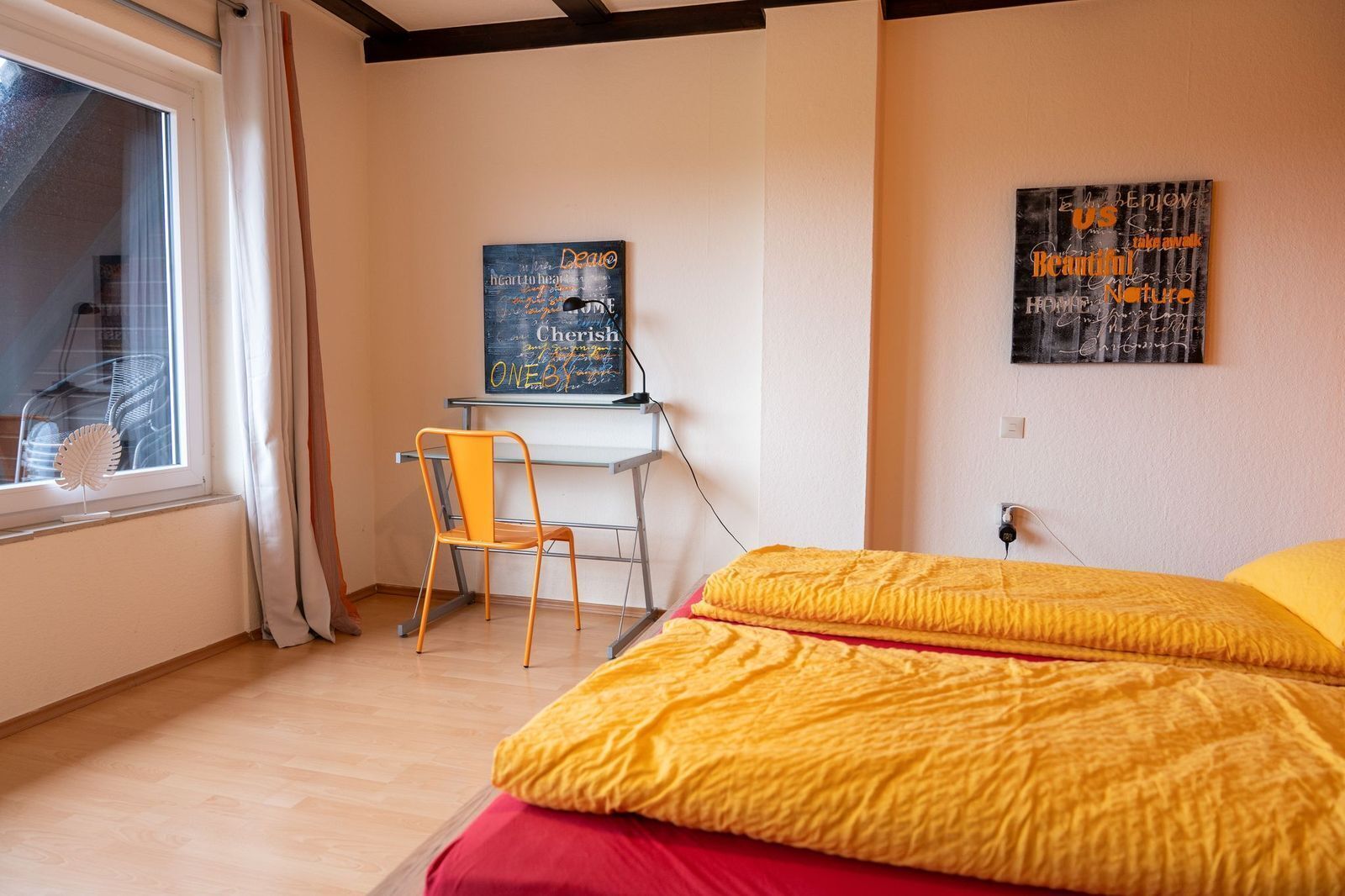 Une chambre avec un lit, un bureau et une chaise. Il y a une fenêtre avec des rideaux, un mur orné d’une affiche et un radiateur.