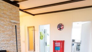 Un salon moderne avec un canapé en cuir noir, un tapis coloré et un fauteuil noir. On peut voir une boîte aux lettres rouge et une horloge sur le mur.