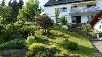 Ein zweistöckiges Haus mit Schrägdach, Balkon und Garten mit verschiedenen Pflanzen und Blumen.