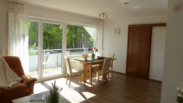 Ein geräumiges Wohnzimmer mit Holzboden, einem Esstisch mit Stühlen, einer Couch und einer großen Schiebeglasdoor, die auf einen Balkon führt.