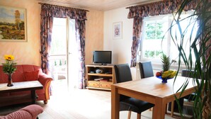 A living room with a sofa, a table, a TV, and a window with curtains.