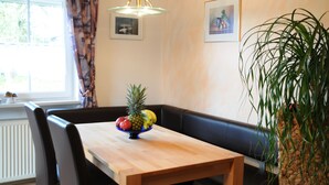 A dining area with a wooden table, black chairs, a fruit bowl, a hanging light fixture, and a potted plant.