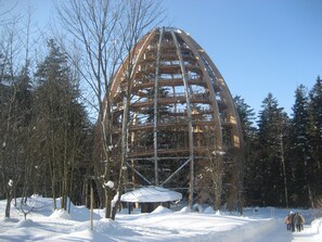 Uma grande estrutura de madeira com um telhado em formato de cúpula, rodeada por neve e árvores.