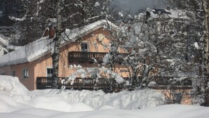 A snow-covered building with a balcony, surrounded by trees and snow.