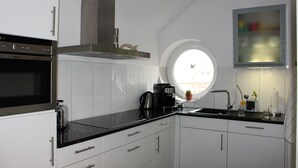 A modern kitchen with white cabinets, a black countertop, a built-in oven, a coffee maker, and a window with a view of the city. - Dünenperle-Borkum, 5 stars, 3 bedrooms, 2 bathrooms, roof terrace (Borkum)