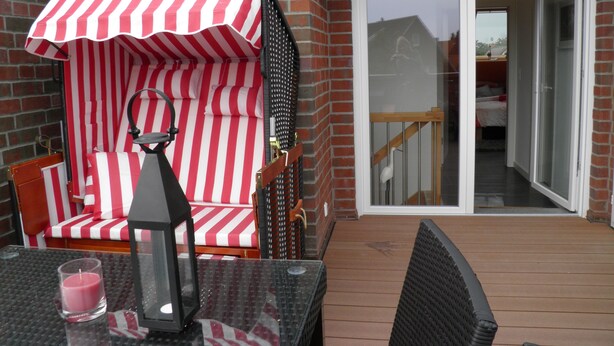 A patio with a red and white striped umbrella, a table with a candle, and a chair. - Dünenperle-Borkum, 5 stars, 3 bedrooms, 2 bathrooms, roof terrace (Borkum)