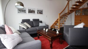 A modern living room with a grey sofa set, a wooden coffee table, and a red rug. A staircase with wooden railings leads to a glass cabinet with decorative items. - Dünenperle-Borkum, 5 stars, 3 bedrooms, 2 bathrooms, roof terrace (Borkum)