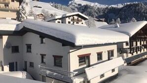 A snow-covered building with multiple balconies, a ski resort in the background, and a mountain range. - Vacation apartment**** with sauna, herbal steam bath, solarium and fitness room (Fontanella)