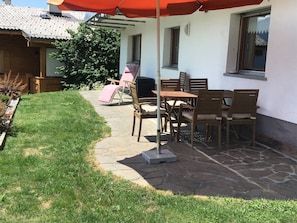 A patio with stone flooring, a table with chairs, and a red umbrella.