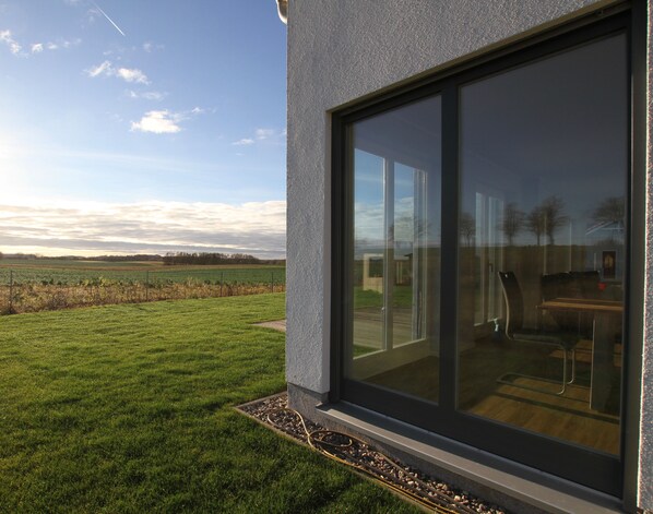 A modern building with large glass windows, a well-maintained lawn, and a view of a field. - A Golden Fall in a Vacation Home with a Fireplace (Barendorf/Dassow)