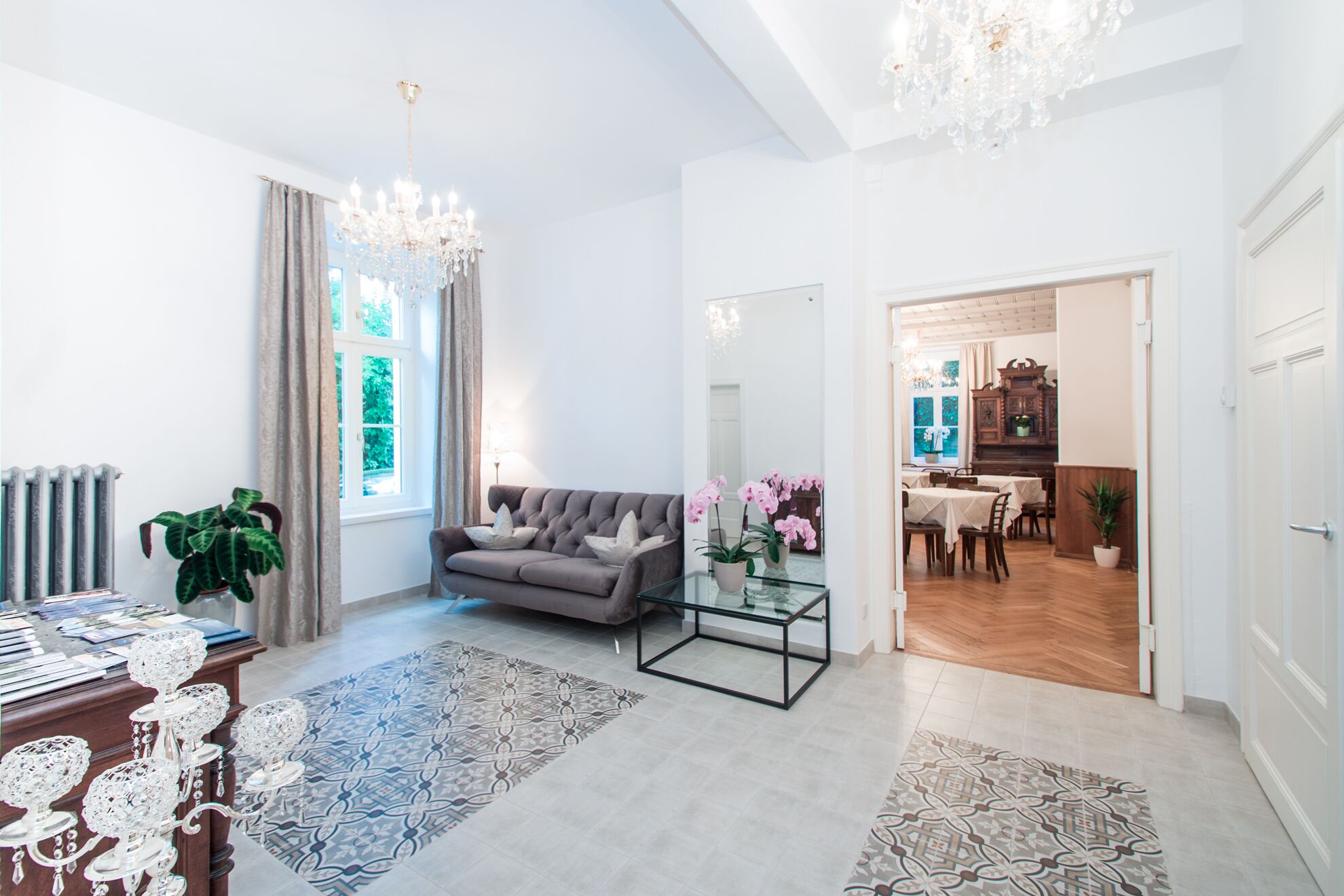 A spacious living room with a grey sofa, a glass coffee table, and patterned rugs.