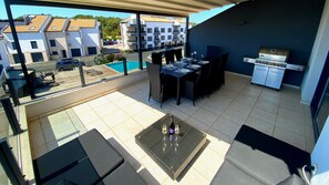 Una terraza en la azotea con zona de comedor, una parrilla y vistas a la piscina.