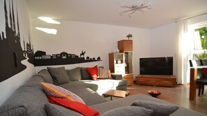 A modern living room with a grey sectional sofa, a flat-screen TV, and a wooden cabinet. - Franconian idyll at Bamberg (Stegaurach)