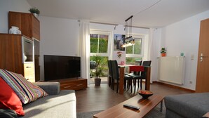 A modern living room with a flat-screen TV, grey sofas, a wooden coffee table, and a dining area with a table and chairs. - Franconian idyll at Bamberg (Stegaurach)