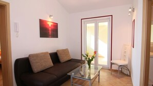Ein Wohnzimmer mit einem braunen Sofa, einem Glastisch, einer Vase mit Blumen und einem weißen Sessel.