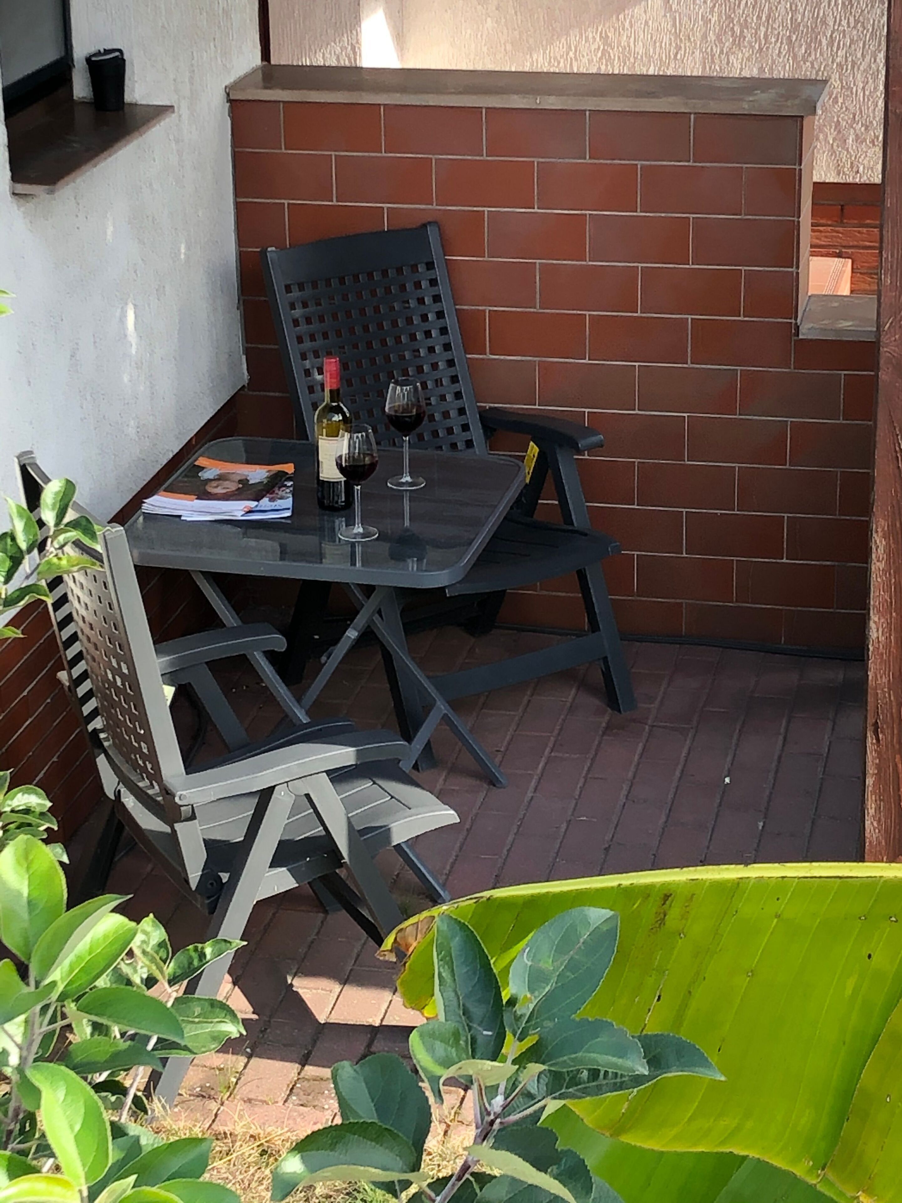 Un espace patio avec une table et des chaises, une bouteille de vin et un verre de vin.